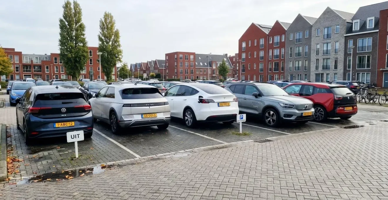 Moderne elektrische en hybride voertuigen geparkeerd op een eigentijdse parkeerplaats in Nederland, met Nederlandse architectuur op de achtergrond.