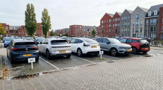 Moderne elektrische en hybride voertuigen geparkeerd op een eigentijdse parkeerplaats in Nederland, met Nederlandse architectuur op de achtergrond.